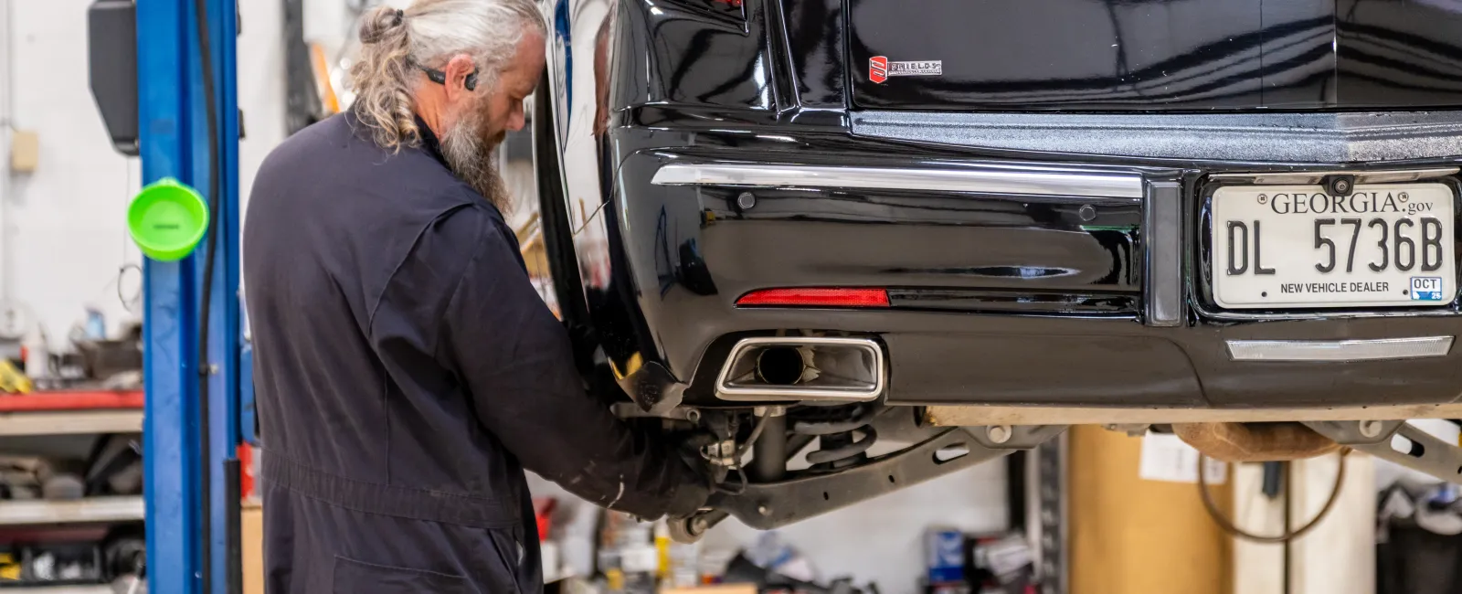 Mechanic with gray hair working on the rear suspension of a black luxury car in a garage workshop
