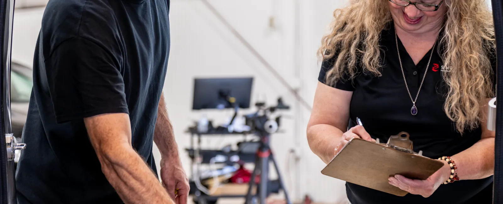 Two workers inspecting and marking metal parts on a table inside an industrial workshop with tools in the background