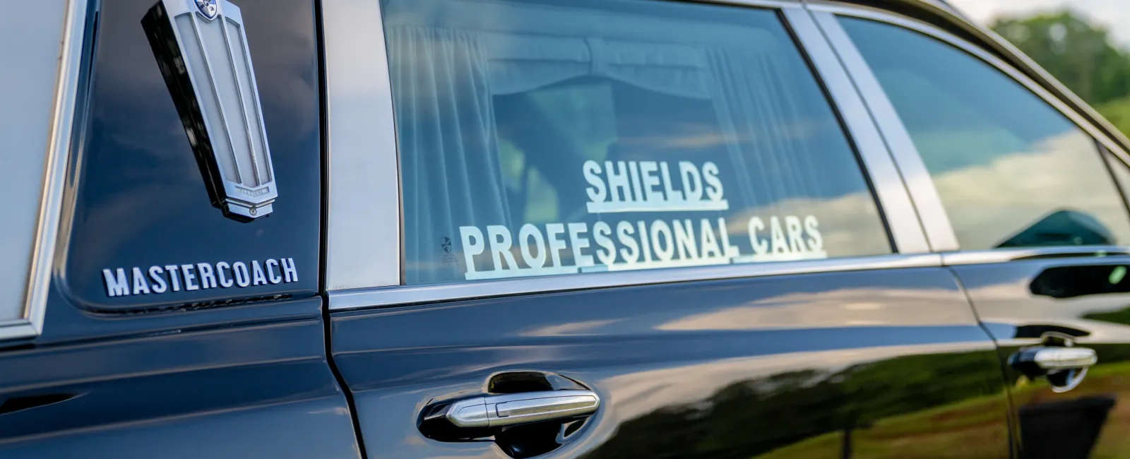 Black Mastercoach vehicle with chrome handle and Shields Professional Cars logo on window in natural outdoor setting
