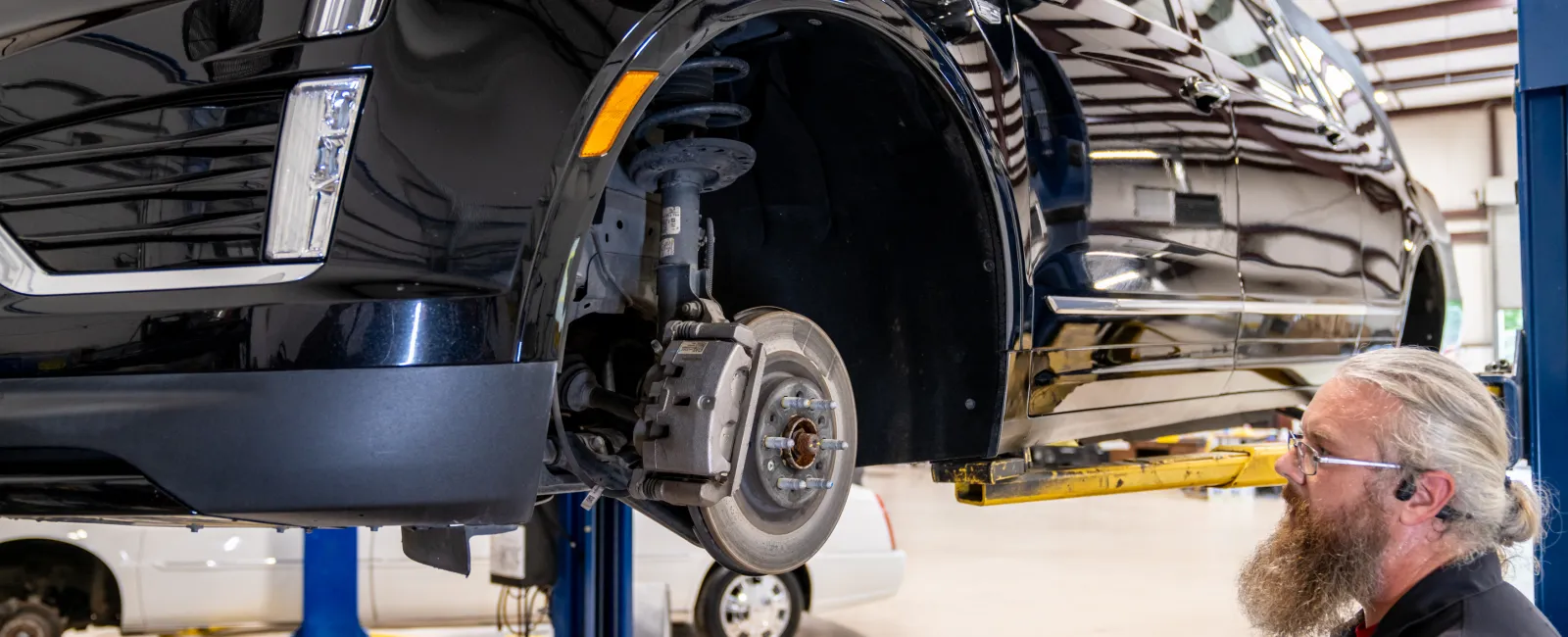 Mechanic inspecting the wheel assembly of a black car lifted in an auto repair shop with removed tire and tools nearby