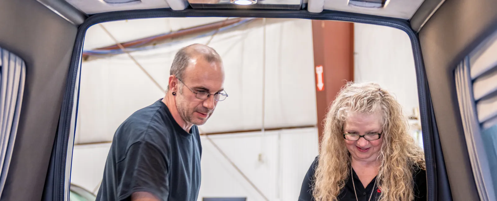 Man and woman inspecting a custom electric skateboard deck layout inside a workshop or garage setting.
