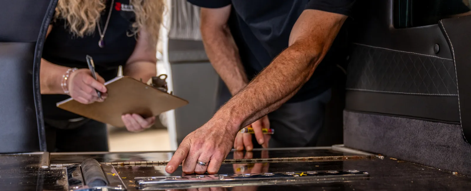 Man pointing at a blueprint on a table while woman with clipboard takes notes in a collaborative workspace