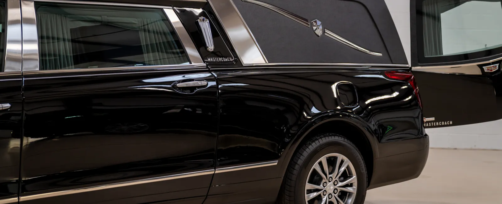 Side view of a black modern hearse with polished wheels and partially opened rear door in an indoor setting
