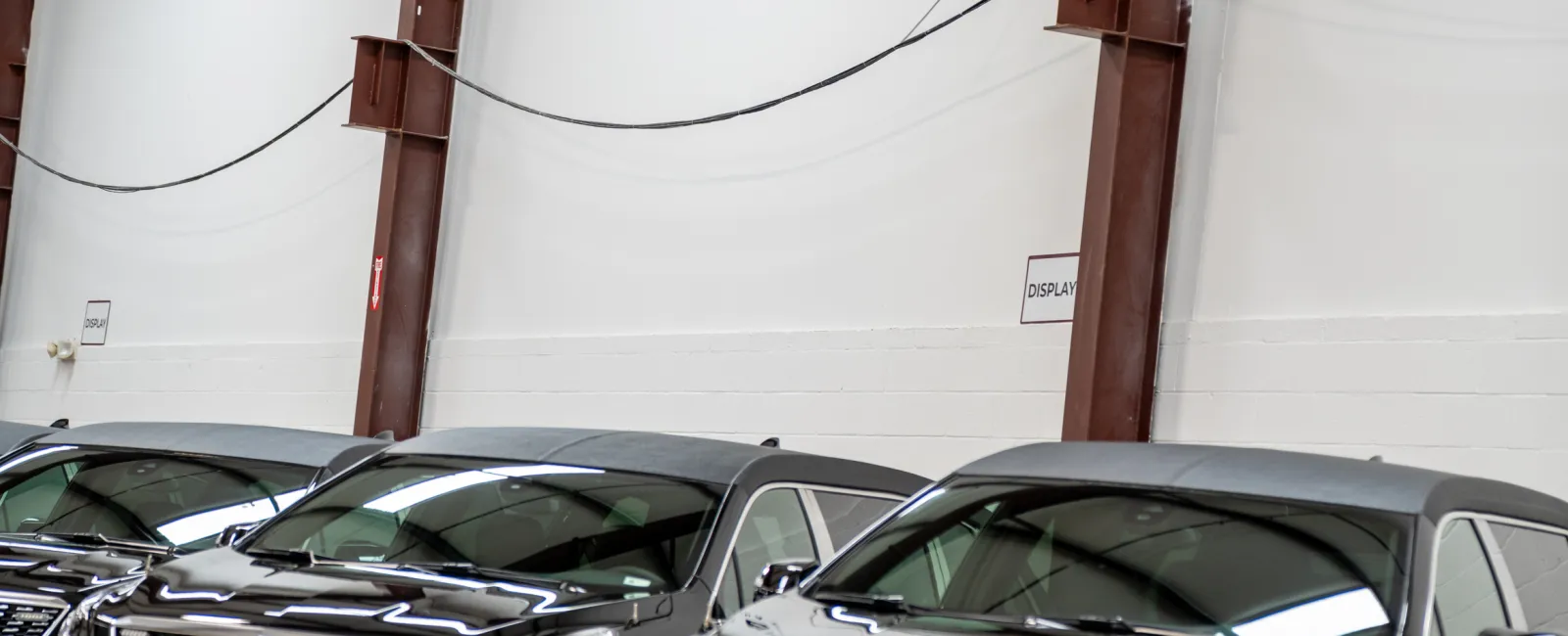 Black Cadillac SUVs lined up inside a spacious dealership garage under Shields Professional Vehicles sign