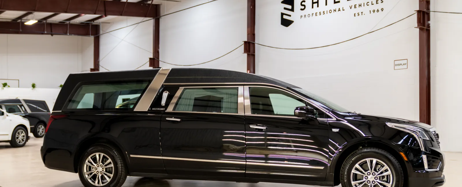 Black professional vehicle hearse displayed indoors at Shields Professional Vehicles showroom with polished floor and bright lighting