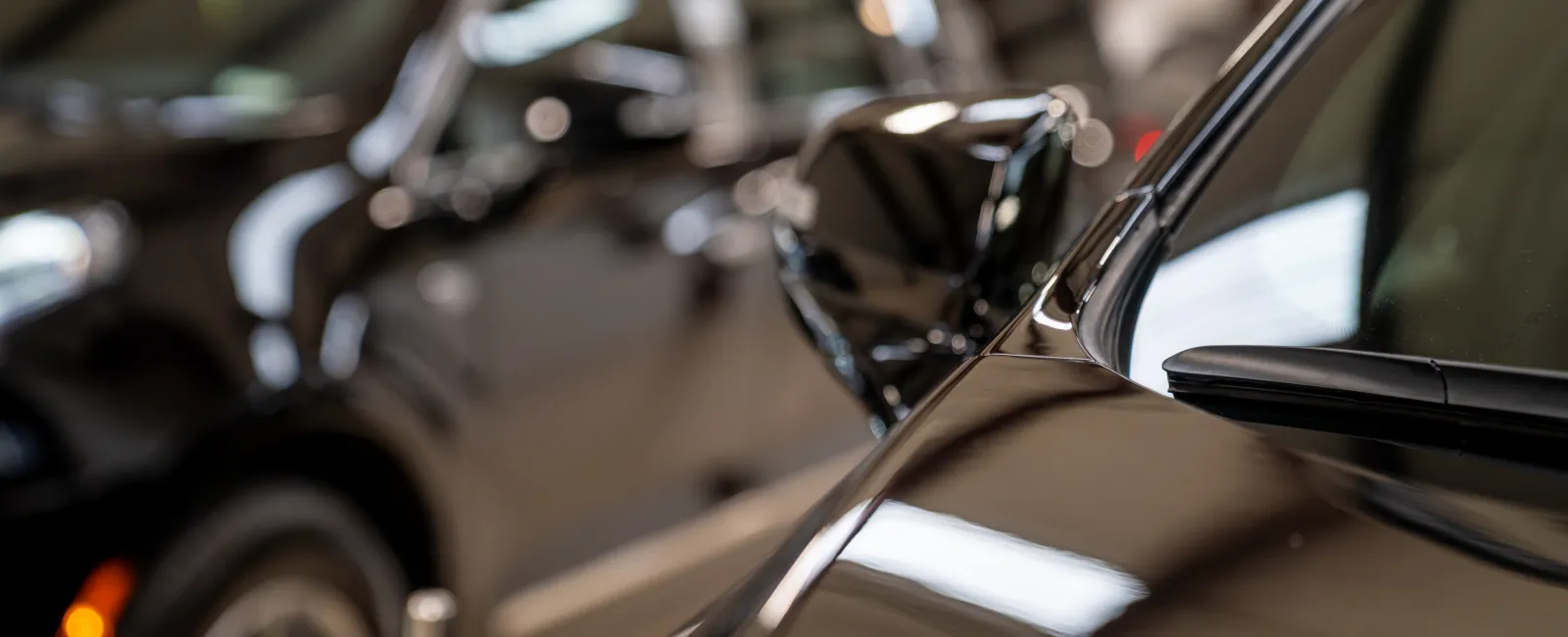 Close-up view of shiny black cars parked indoors highlighting side mirrors and reflective surfaces under soft lighting