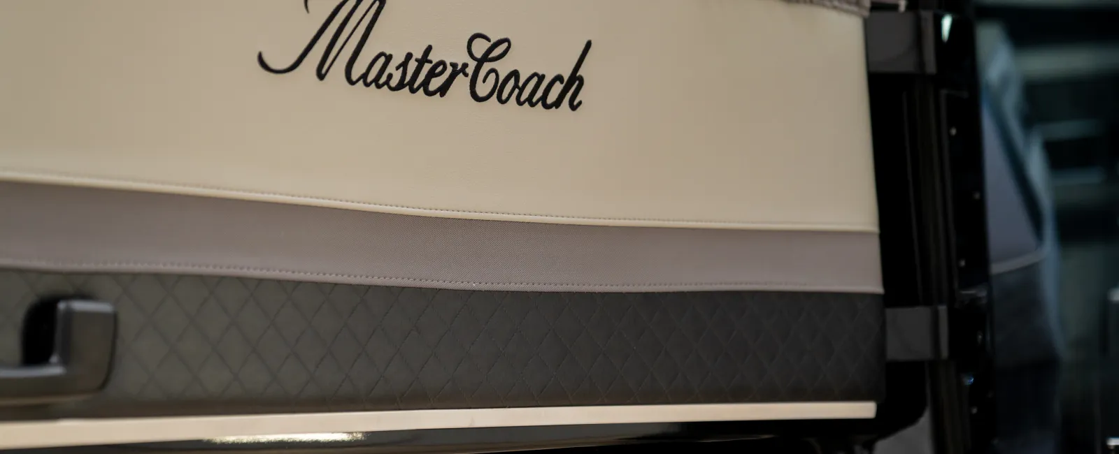 Close-up of a MasterCoach logo on a beige and brown luxury vehicle door interior with diamond stitching details