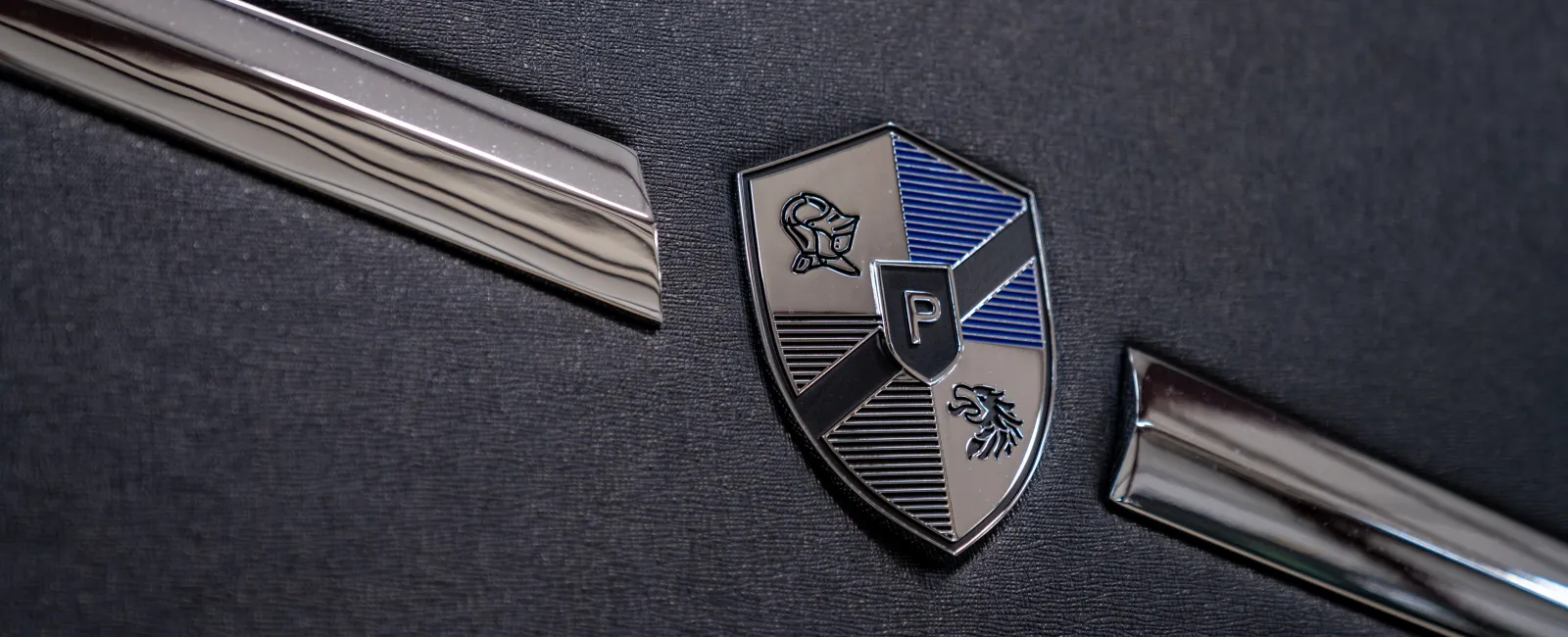 Metallic shield emblem with a knight and lion on a black textured background between chrome trim.