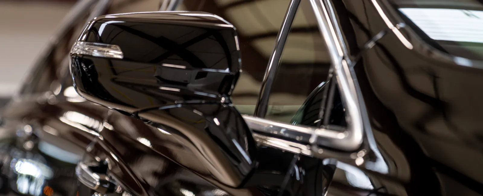 Close-up of a glossy black car side mirror and door with reflective metallic surfaces in a showroom.