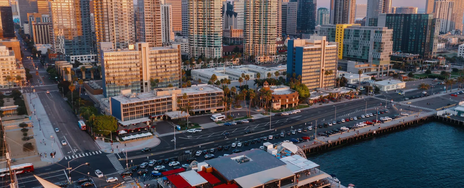 Aerial view of San Diego waterfront with pier restaurants and tall city skyscrapers at sunset.