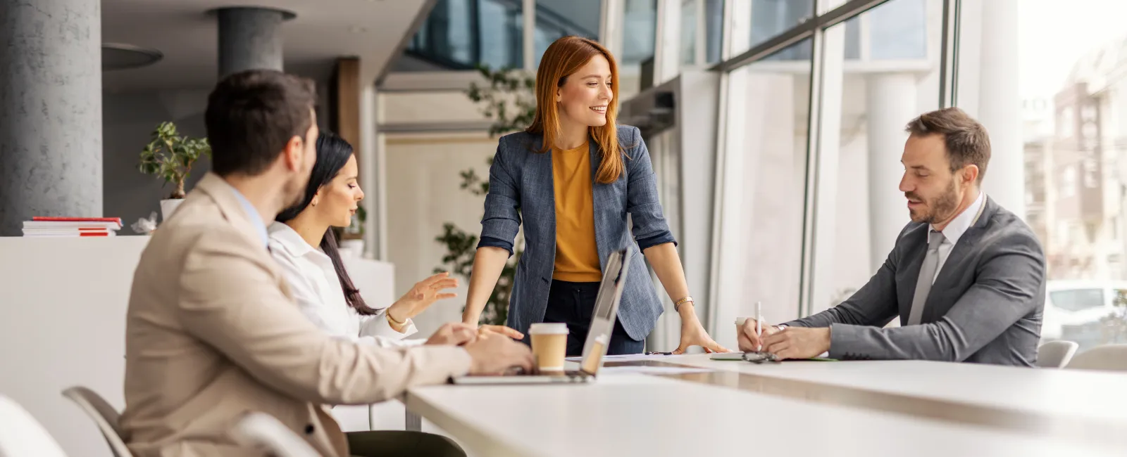 Four business professionals collaborating in a modern office with large windows and natural light.