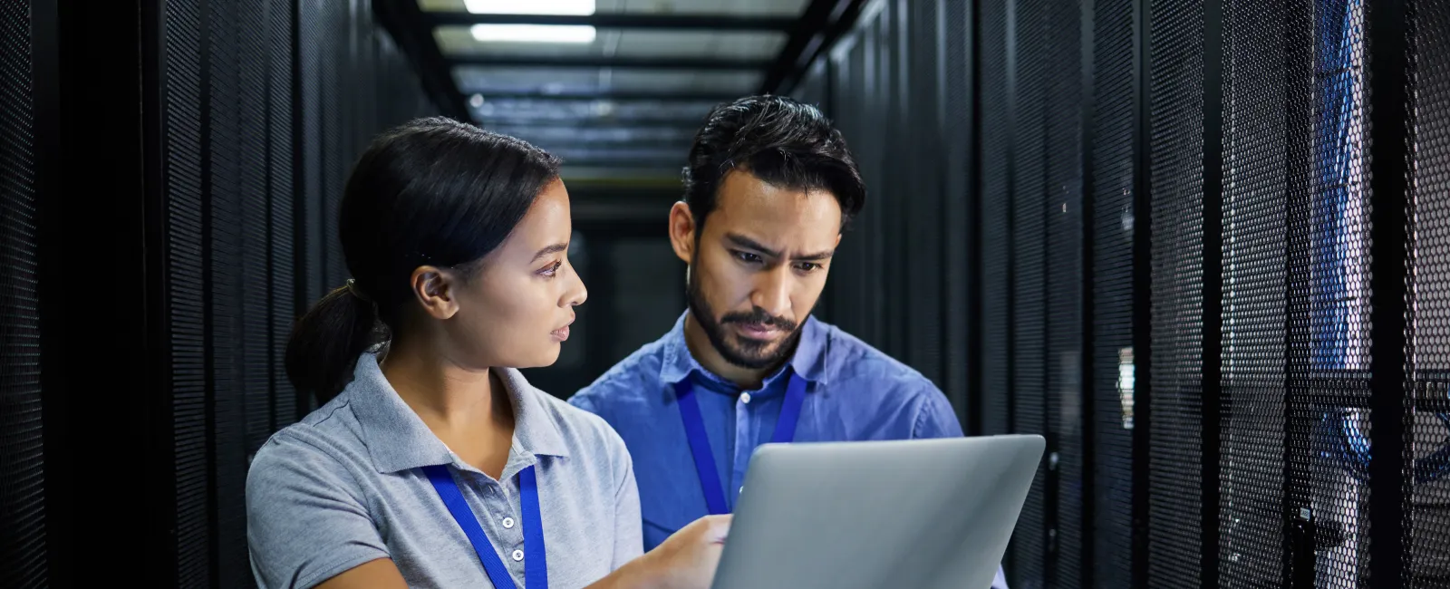 Two IT professionals inspecting data center servers while discussing information on a laptop in a server room.