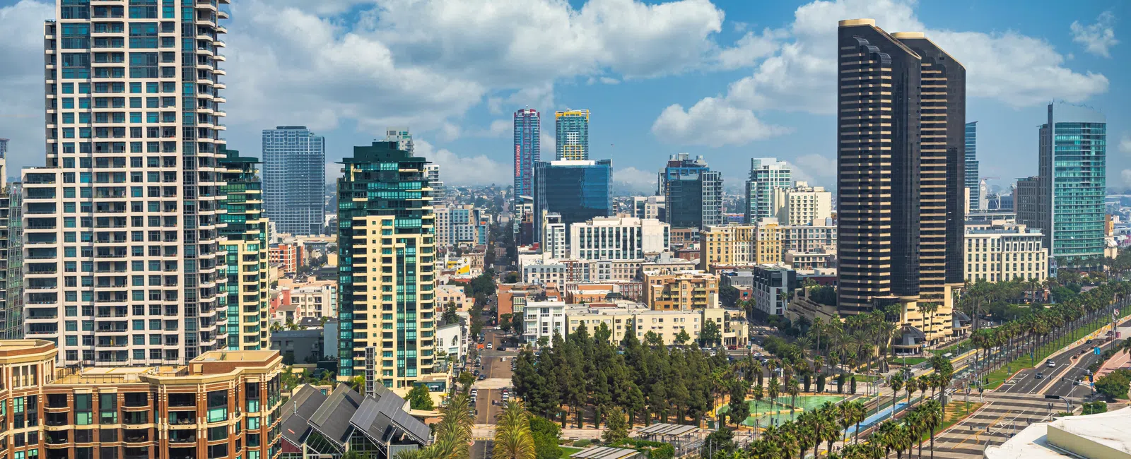 Downtown cityscape with modern skyscrapers, palm-lined streets, and clear blue skies with clouds.