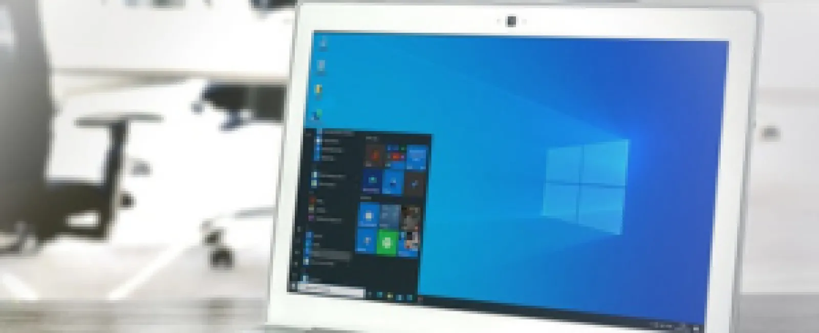 Silver laptop with Windows 10 start menu open on screen in bright modern office setting