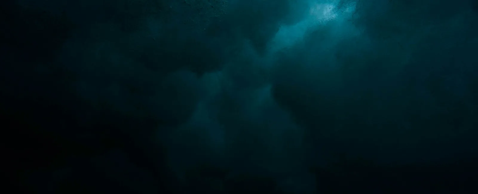 Dark underwater scene with deep blue light filtering through turbulent water and bubbles.