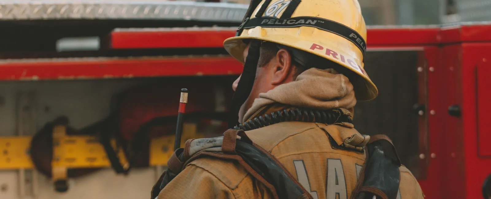 Firefighter in protective gear and helmet with oxygen tank stands near red fire truck in daylight.