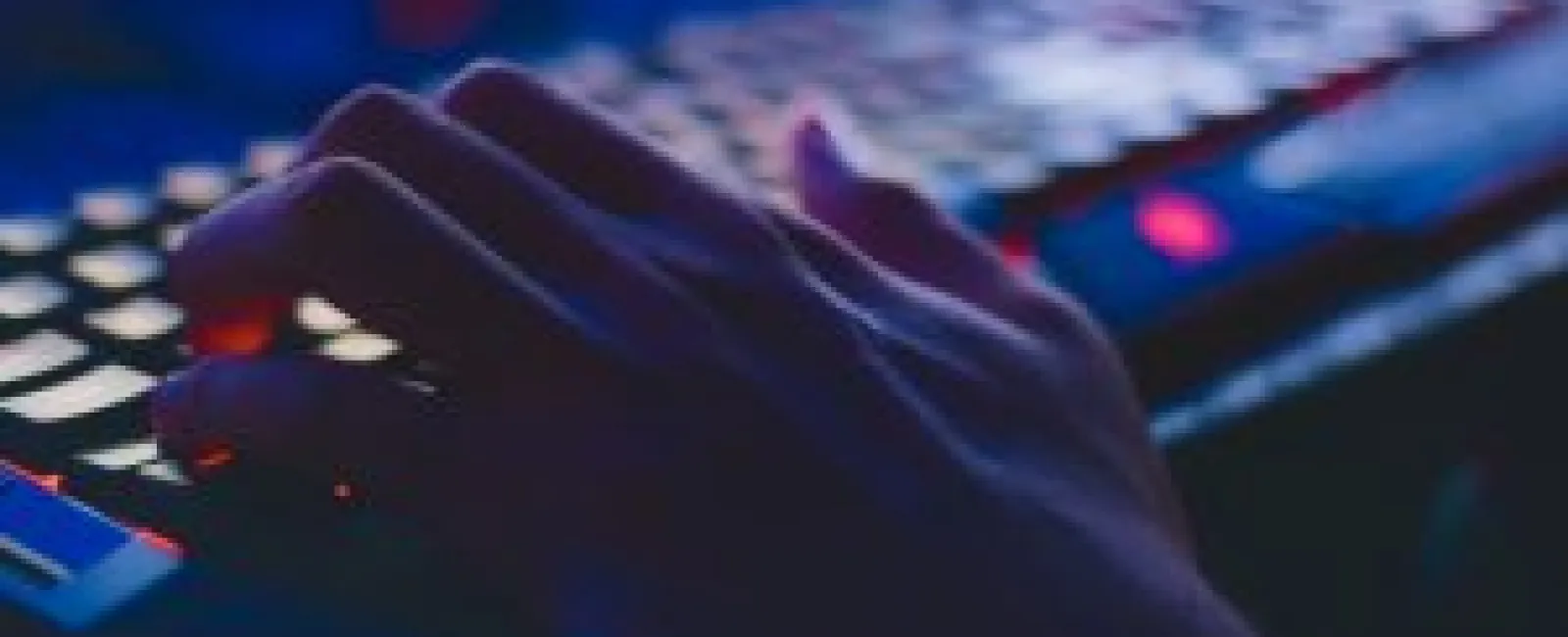 Close-up of hand typing on a keyboard with colorful backlit keys in low light environment.