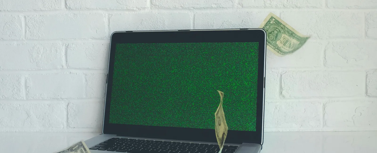 Laptop with green digital code on screen and floating dollar bills around, symbolizing digital finance or hacking.