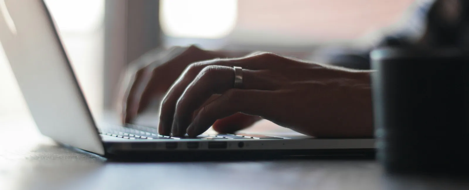 Close-up of hands typing on a laptop keyboard in soft natural light on a wooden table.