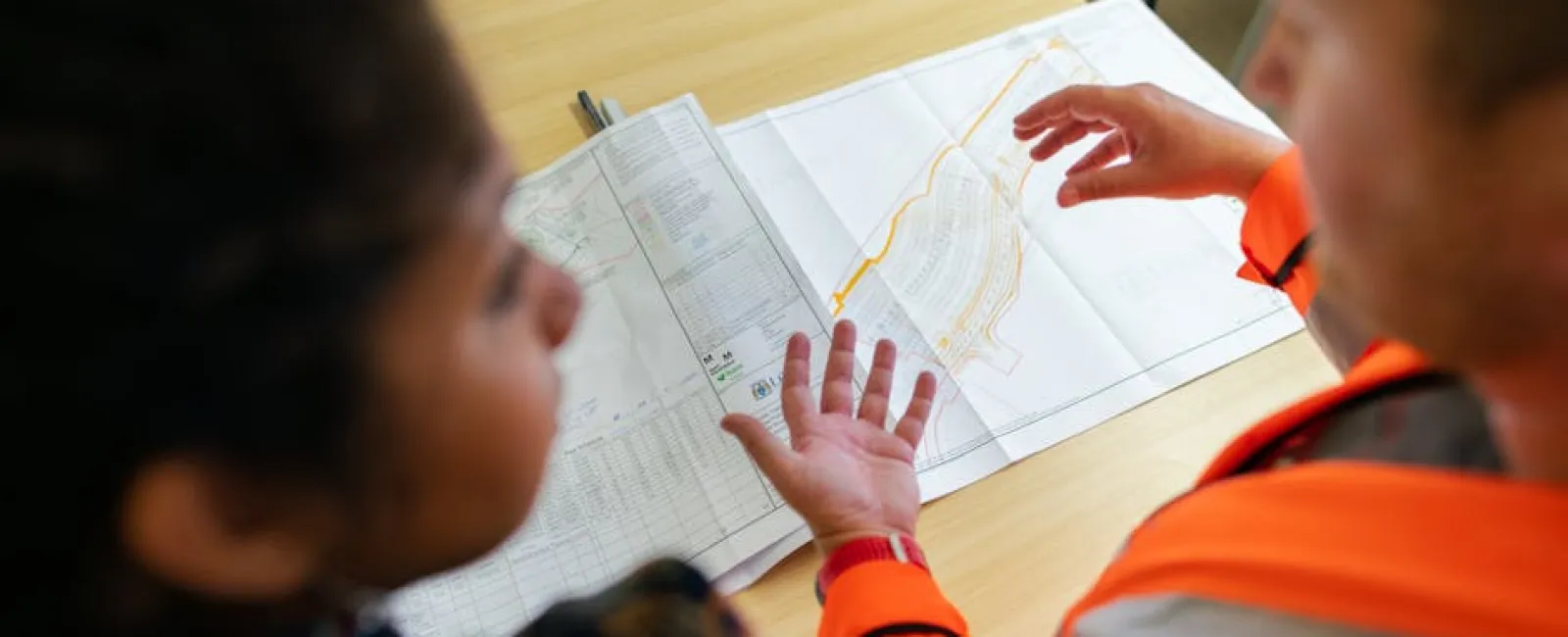 Two professionals reviewing detailed architectural plans on a wooden table in an office setting.