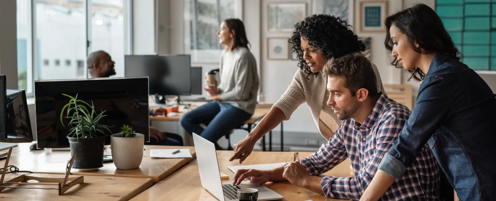 Team of professionals collaborating over a laptop in a modern office with natural light and plants.