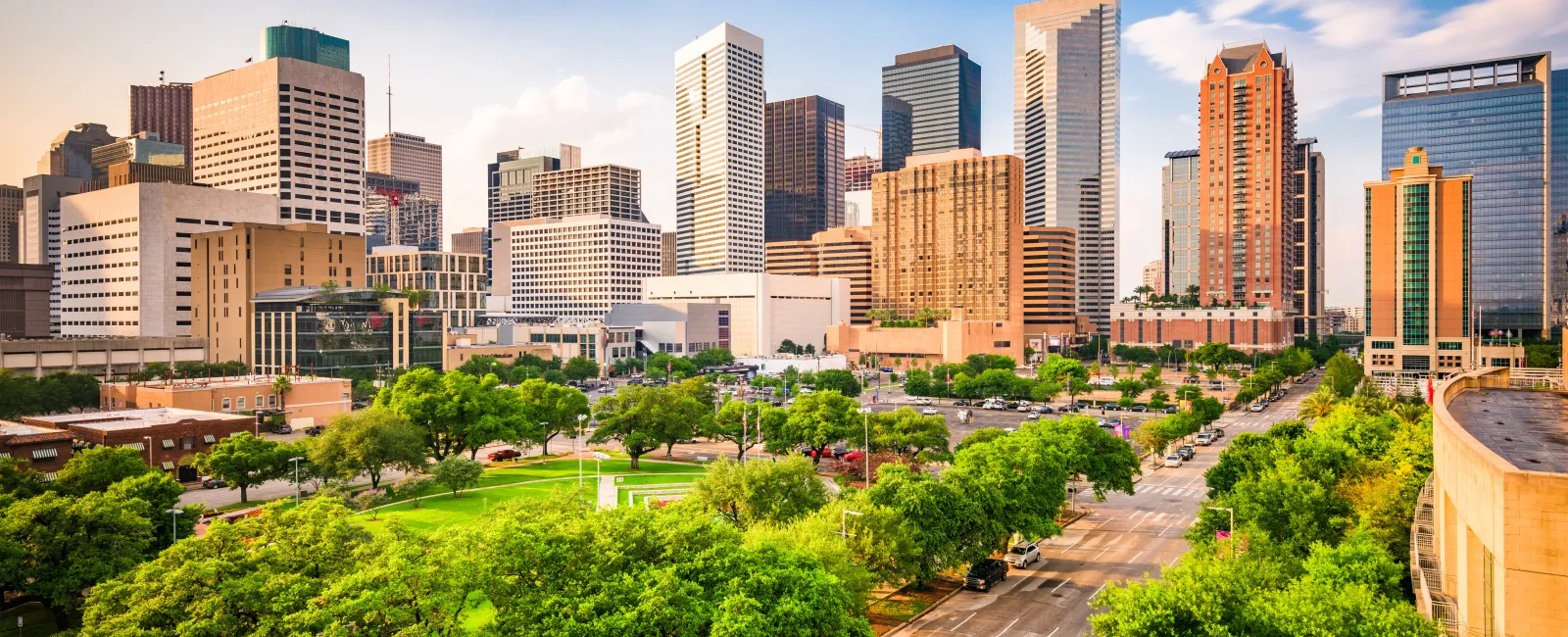 Sunny day view of a city skyline with tall buildings and a green park in the foreground