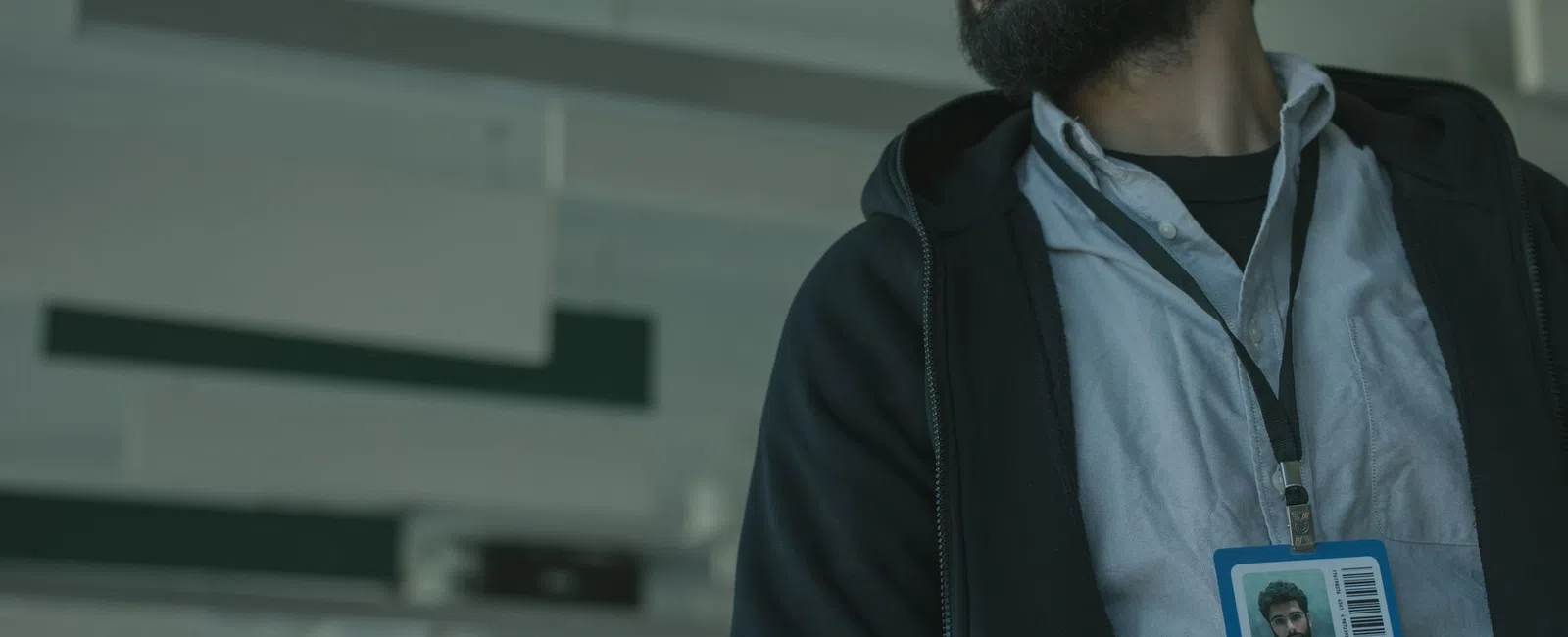 Bearded man wearing glasses and ID badge in an office setting looking to the side.