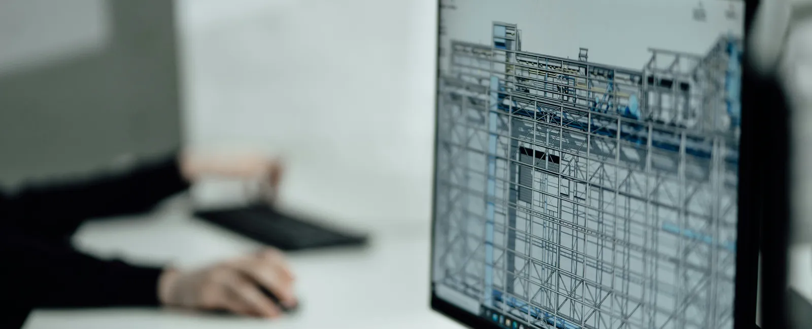 Person working on a computer with a 3D architectural design model in a program like AutoCAD displayed on the monitor screen.