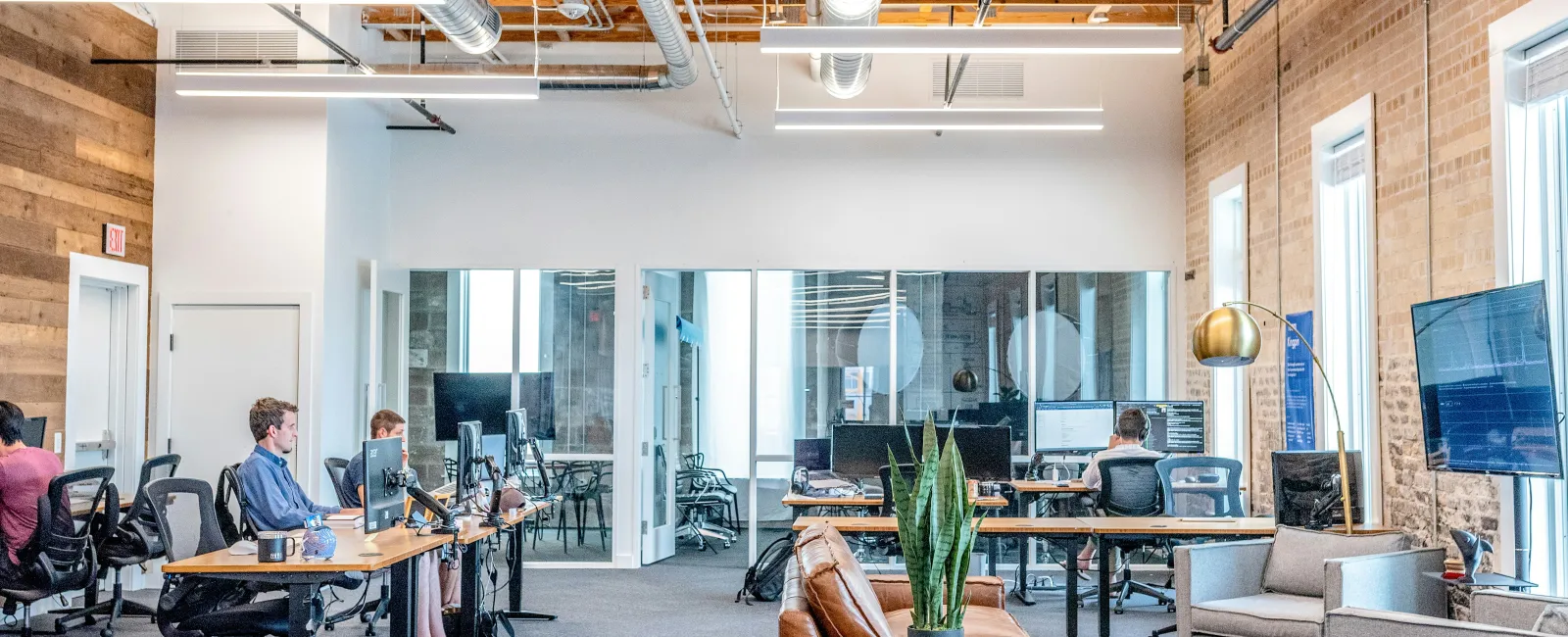 Modern open office space with wood ceiling, exposed ducts, desks, computers, and collaborative seating areas