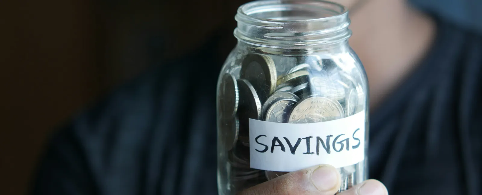 Close-up of person holding a glass jar filled with coins labeled savings for financial planning.