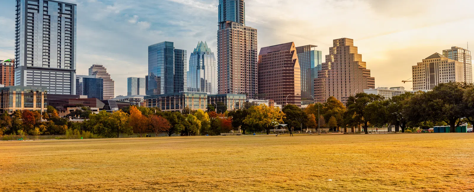 Austin skyline with modern skyscrapers and autumn trees under a partly cloudy sky at sunset.