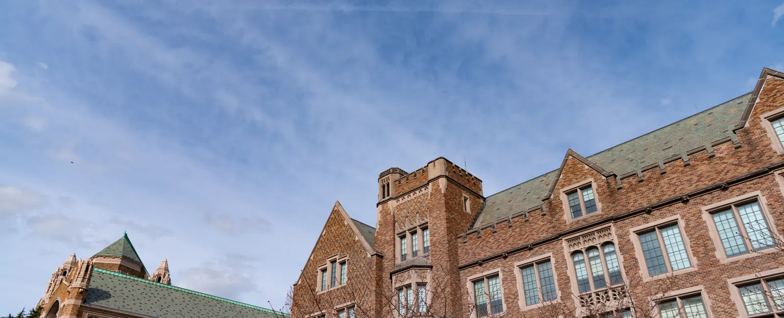Historic university buildings with stone facades and green roofs under a blue sky with scattered clouds.