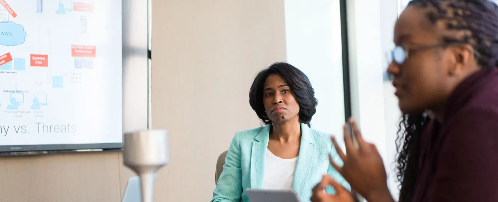 Two women engaged in a business meeting with laptops and a presentation screen showing a strategy diagram.