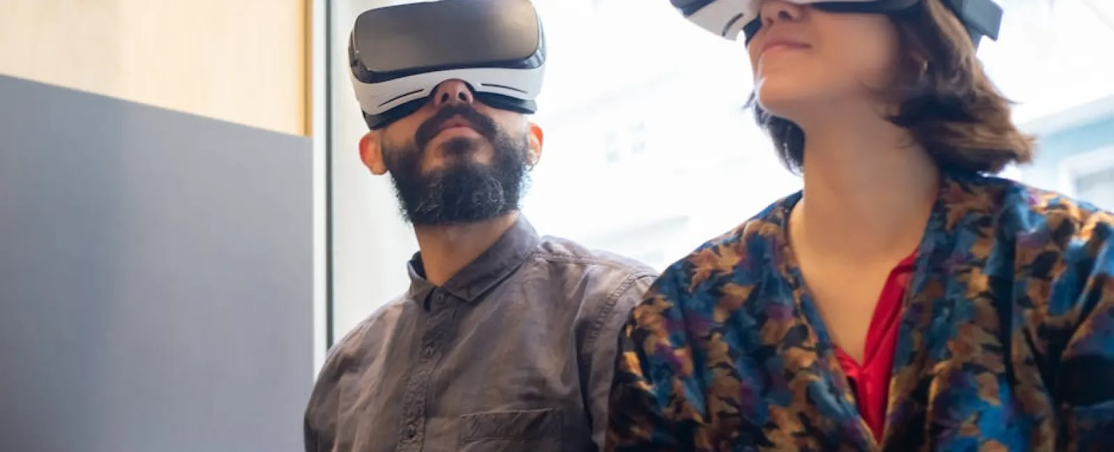 Man and woman wearing virtual reality headsets indoors near window exploring VR experience.