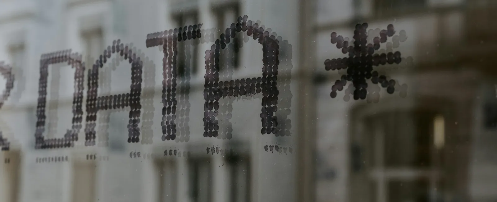 The word DATA* formed with small black dots on a glass window with a reflective city background.