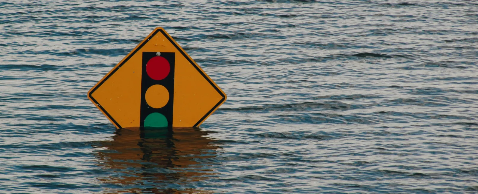 Flooded area with a traffic signal warning sign partially submerged in water.
