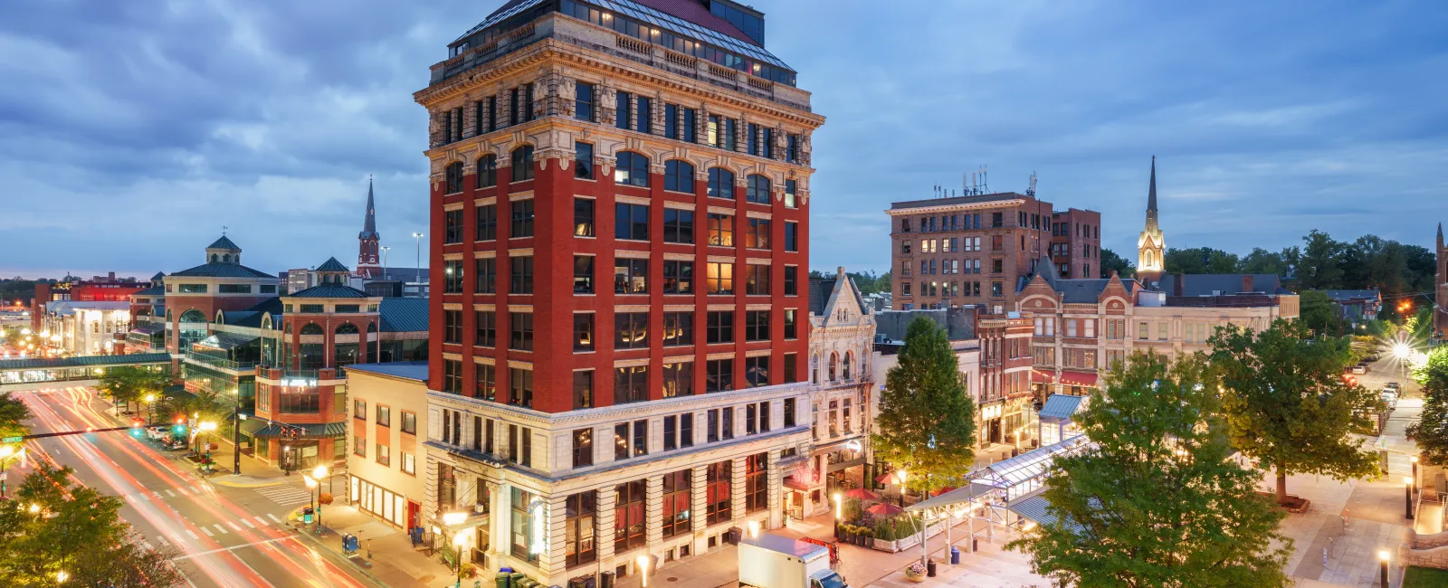 Historic red brick building on busy city street at twilight with light trails and lit storefronts.