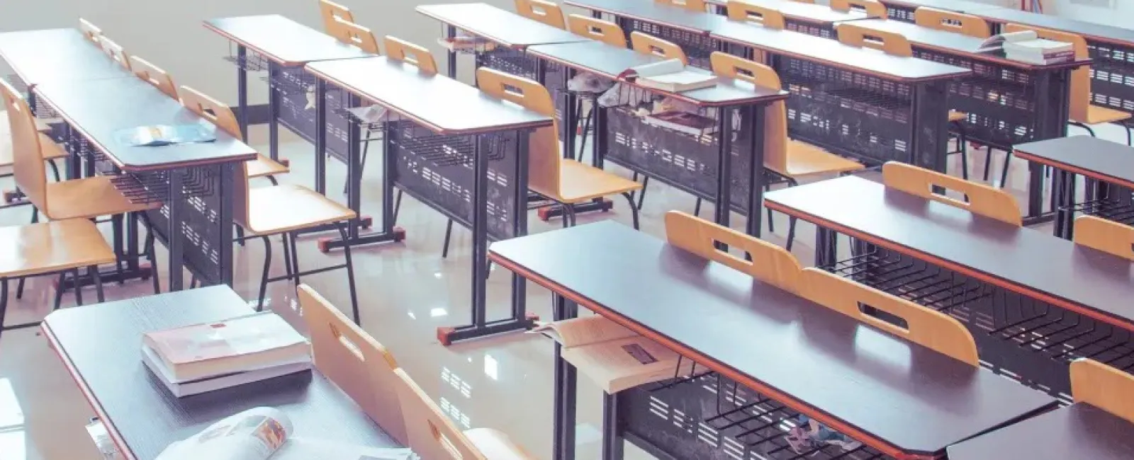 An empty classroom filled with desks. One desk has a various books on it.