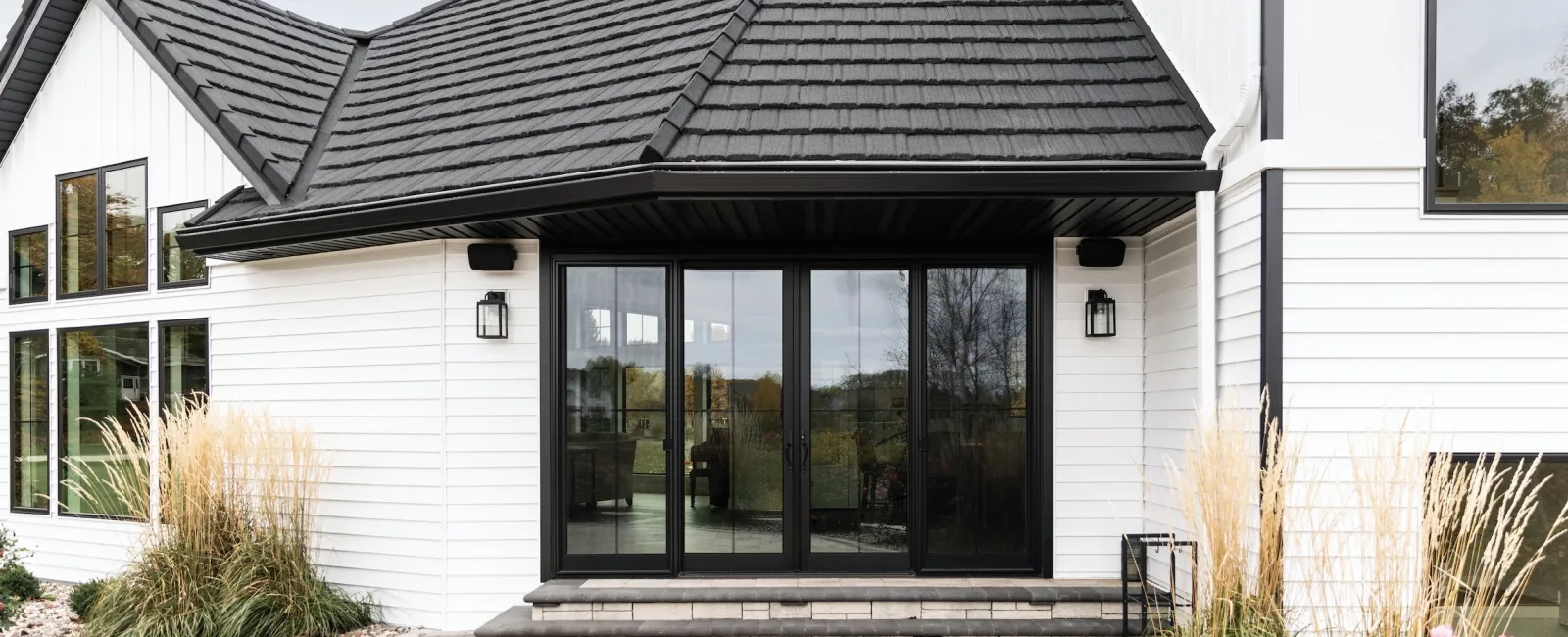 Modern white house exterior with black roof and large sliding glass doors opening to patio area.