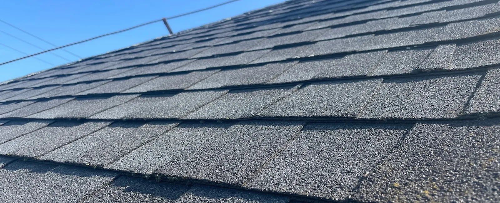 Close-up of a gray asphalt shingle roof against a clear blue sky.