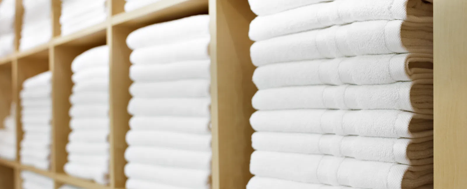 Neatly stacked white towels organized on wooden shelves in a clean storage area.