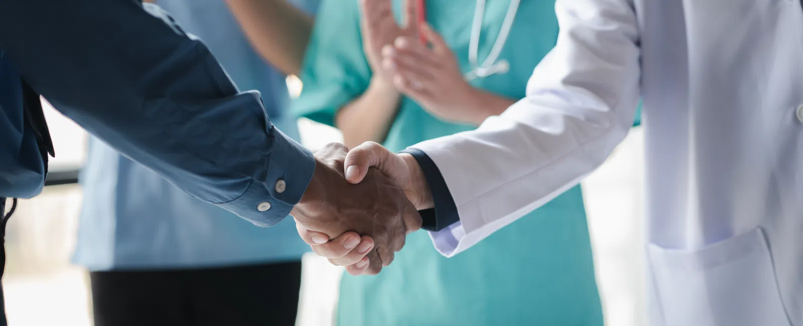 Doctor and patient shaking hands with medical staff applauding in background in healthcare setting.