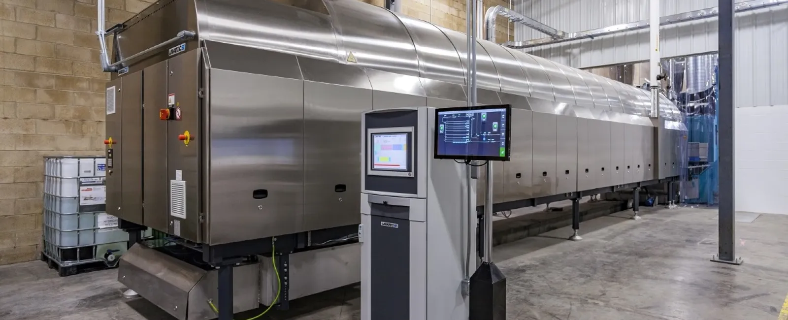Large stainless steel industrial food processing machine with control panel in a clean factory setting