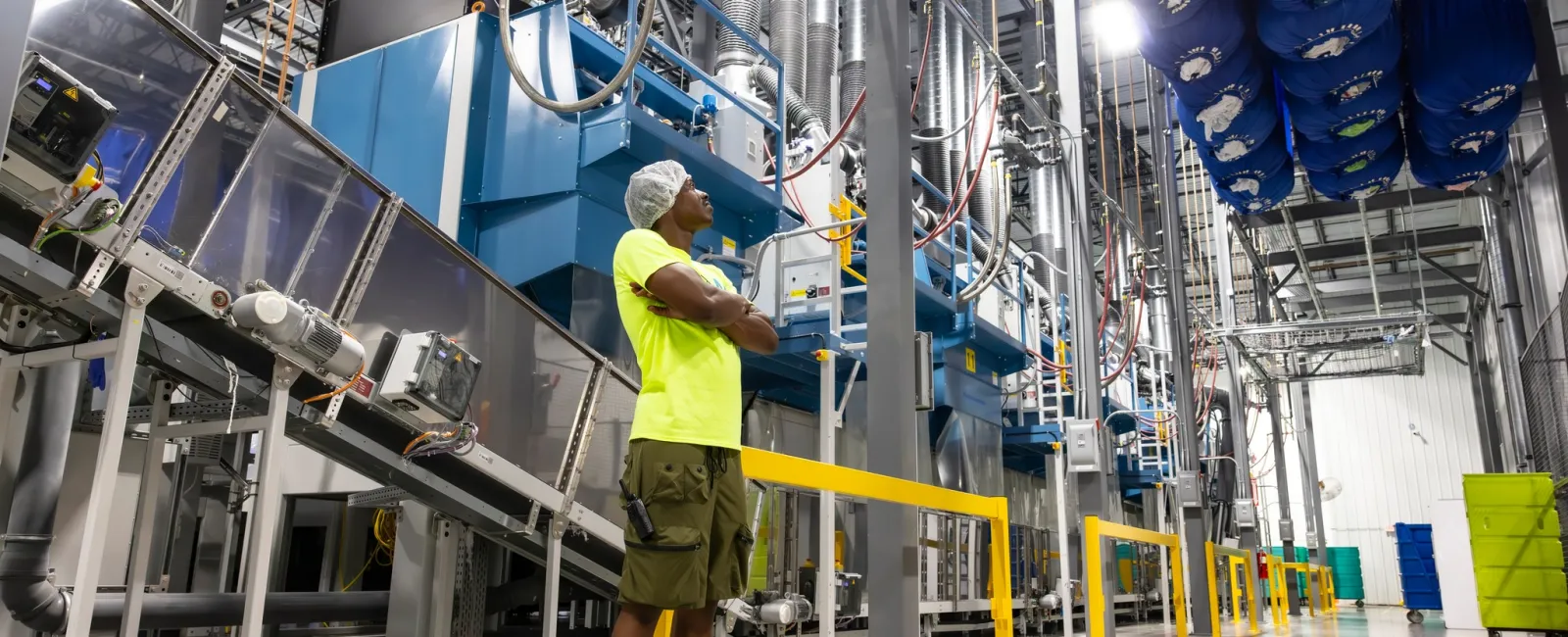 Worker in safety gear inspects large industrial machinery inside a bright, clean manufacturing facility.