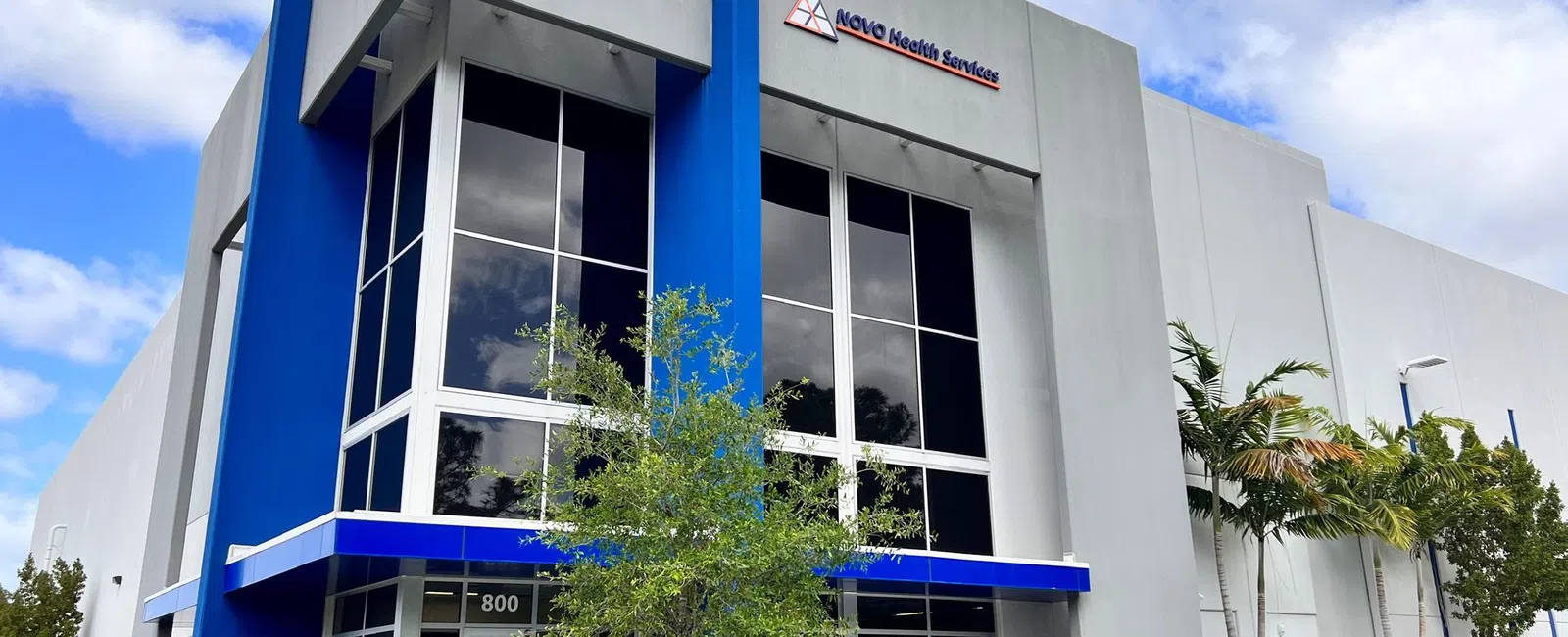 Modern commercial building with blue accents and large windows under a partly cloudy sky.