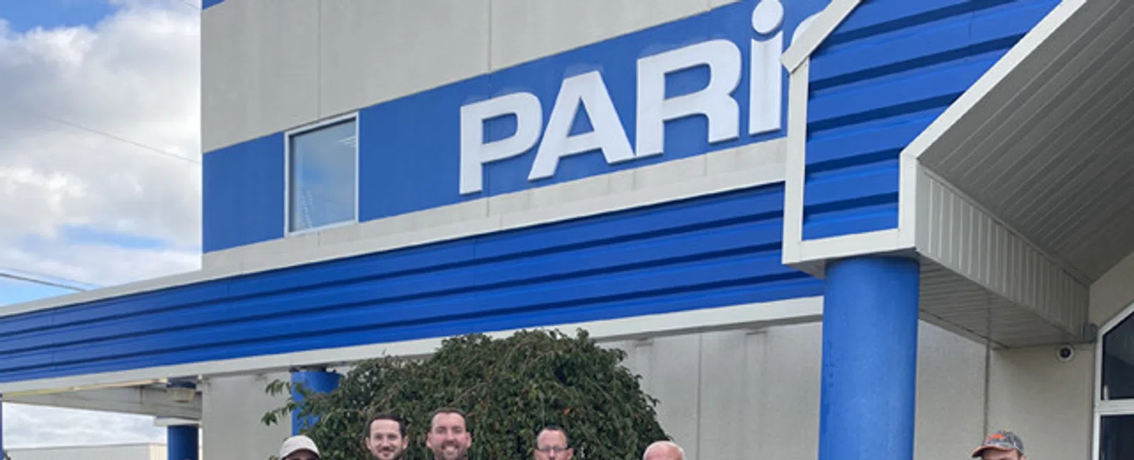 Group of employees standing outside a building with PARI sign and blue accents under a cloudy sky