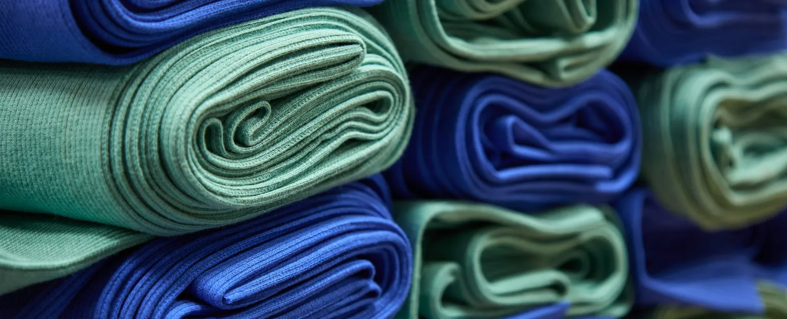 Close-up of neatly rolled blue and green fabric towels stacked in rows, showing texture and color contrast