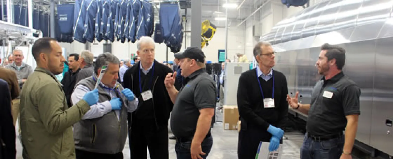 Group of men discussing and examining equipment in an industrial factory setting with hanging garments.