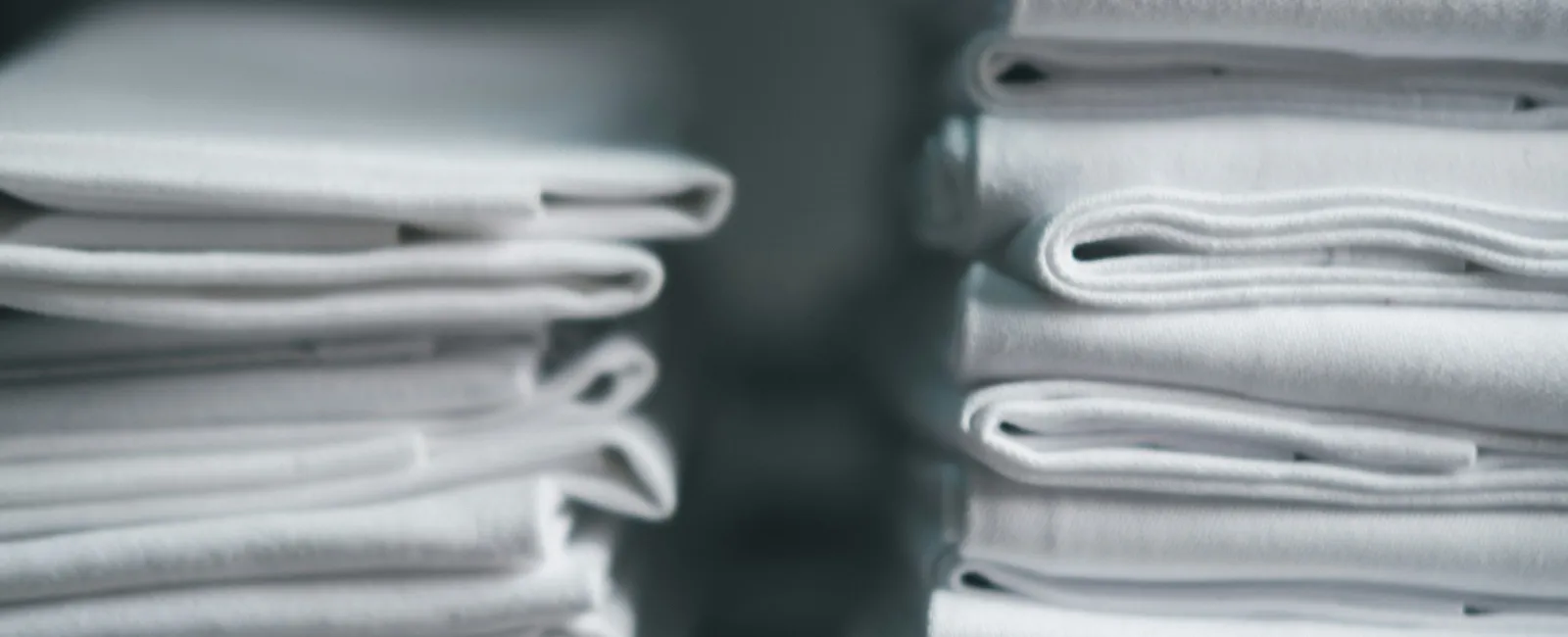 Stacks of neatly folded white fabric towels arranged closely with soft lighting.