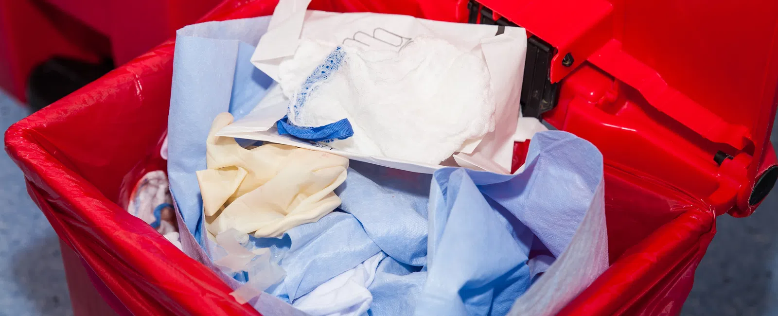 Red biohazard waste bin filled with used medical gloves and disposable protective materials.